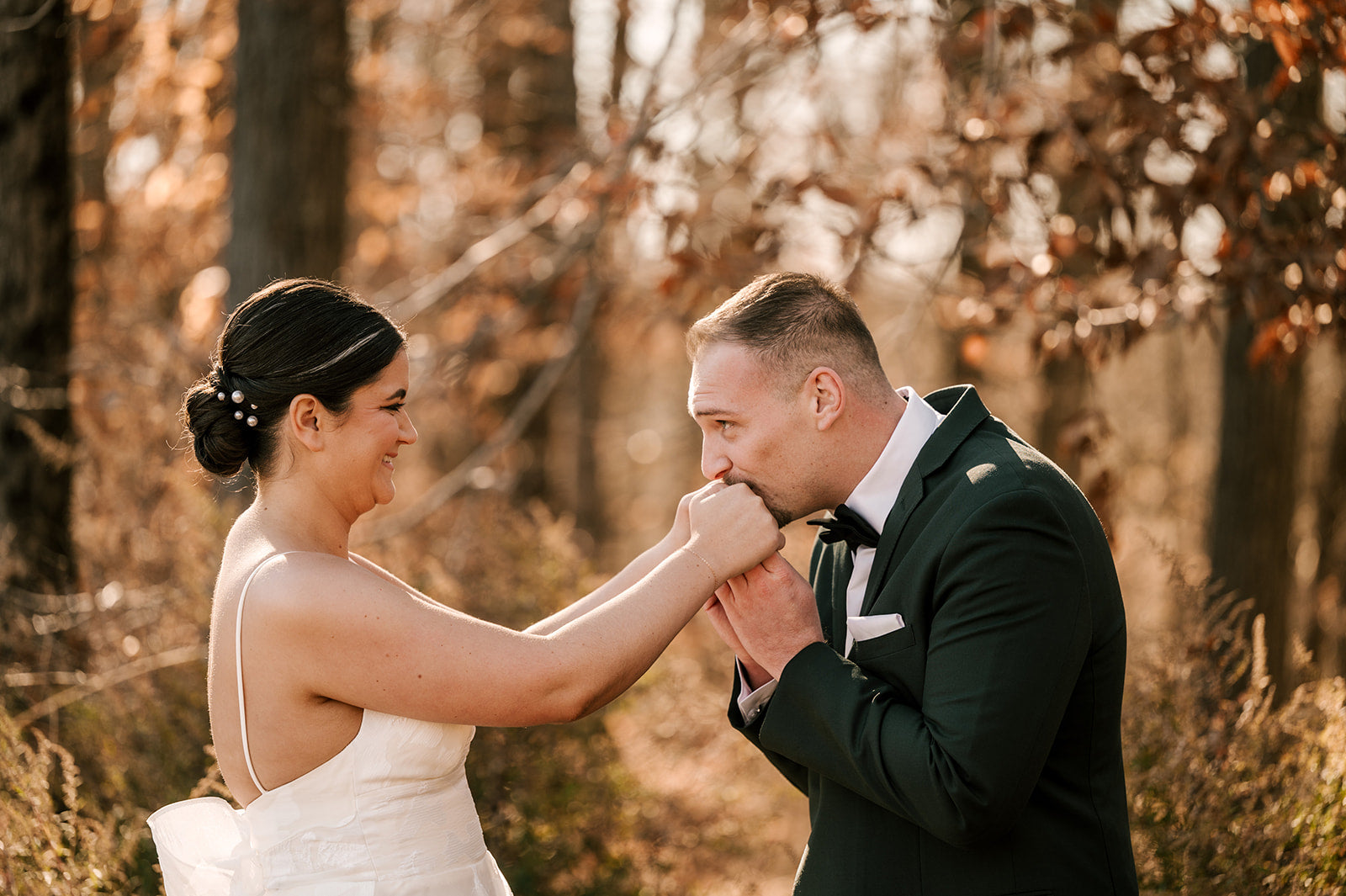 Couple in wedding attire standing close together in a forest setting.