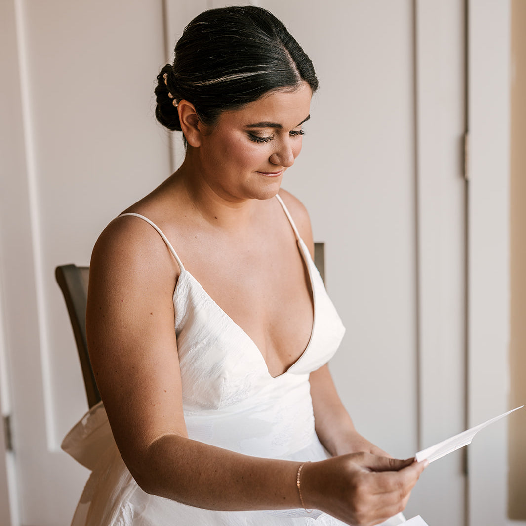 Woman in a white dress holding a piece of paper against a neutral background wearing Permanent Jewelry