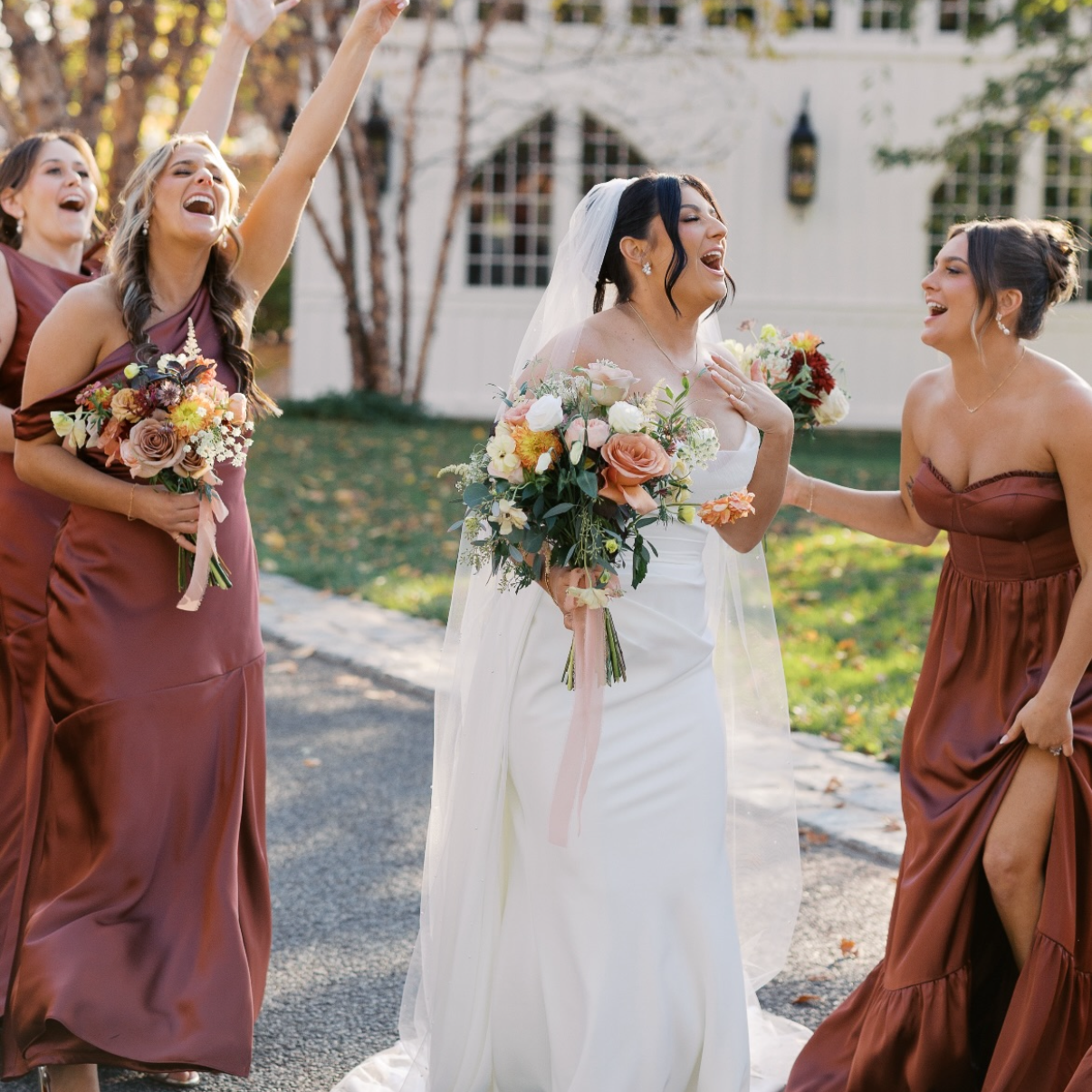 Bride with bridesmaids in brown dresses in front of a white building.
