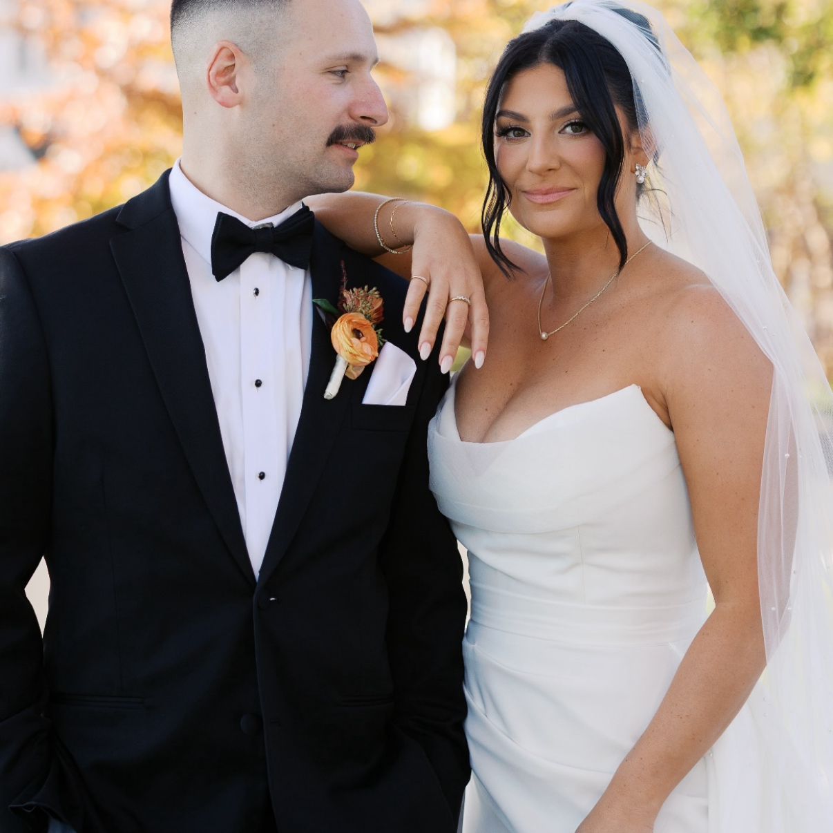 Man in a tuxedo and woman in a wedding dress standing together outdoors.